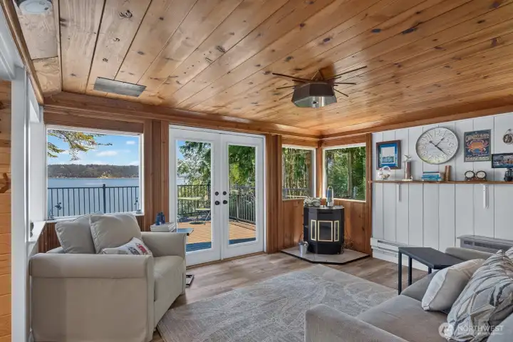 Warm and inviting living room featuring panoramic water views, a cozy pellet stove, and French doors that open to the expansive deck.