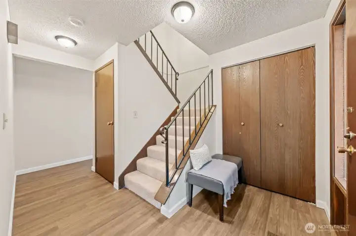The entryway includes laminate hardwood flooring and neutral finishes for a clean, timeless look. Double coat closets and a carpeted staircase offer functionality, with a door leading to additional storage under the stairs.