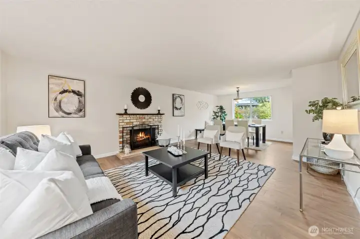 The inviting living room showcases a wood-burning fireplace with a chic mantel, rich laminate floors, and a flow to the kitchen, dining area, and entryway. Its open layout creates a warm and connected   space for both relaxing and entertaining.