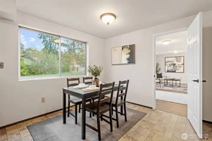 The breakfast table comfortably seats four, creating a welcoming space for casual meals and conversation. A large front window brings in balanced natural light and frames a view of the outdoors.