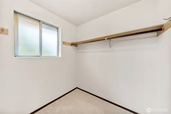 The primary suite closet offers generous hanging space and natural light from a frosted window. Neutral finishes and new carpet create a clean, functional storage area.