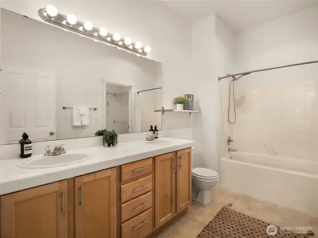 Primary bathroom with dual vanity sinks and a walk-in closet to the right of the bathtub
