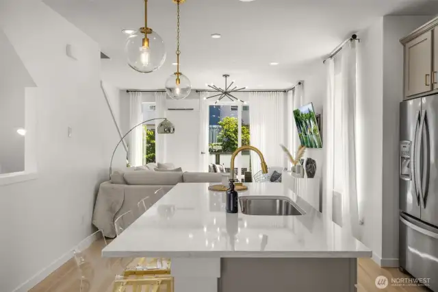 Quartz island with gold fixtures, and pendent lighting, opens to living and dining