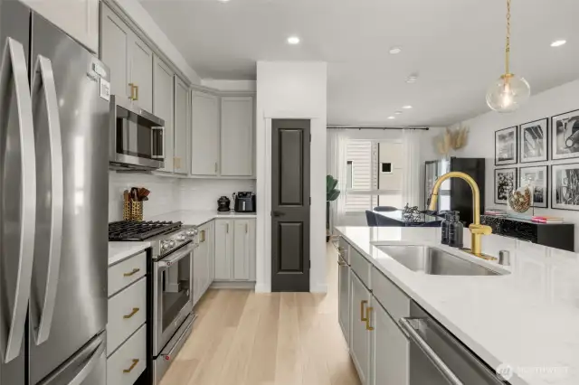 Quartz island with gold fixtures, and pendent lighting, opens to living and dining