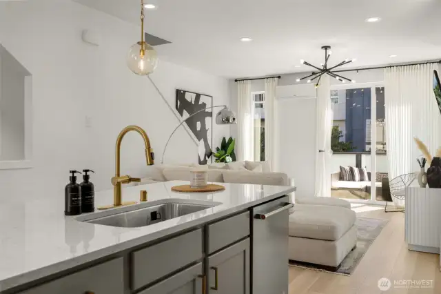 Quartz island with gold fixtures, and pendent lighting, opens to living and dining