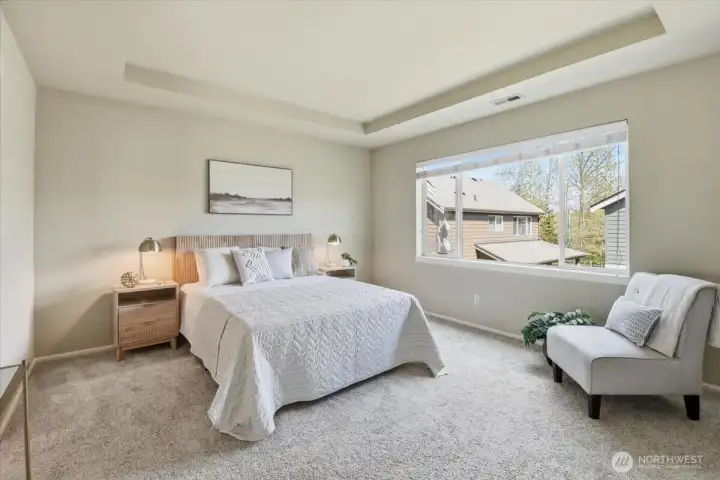 Spacious primary bedroom with tray ceiling, large picture window, and soft natural light creating a peaceful retreat.