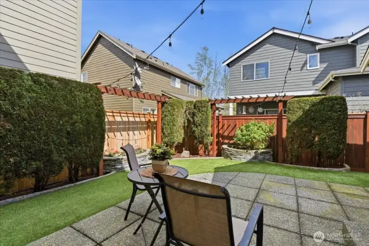 Fully fenced backyard patio with low-maintenance landscaping, string lights, and space for outdoor dining and entertaining.