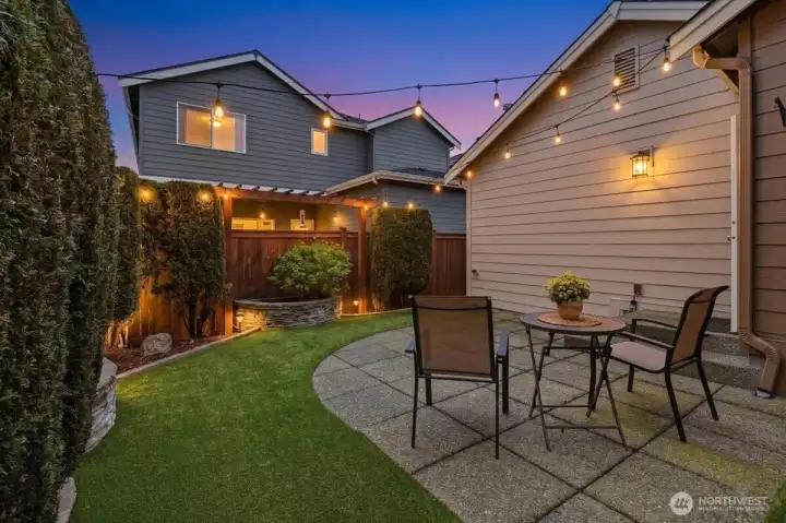 Evening view of the side patio and yard with glowing exterior lighting, showcasing inviting outdoor living after sunset.