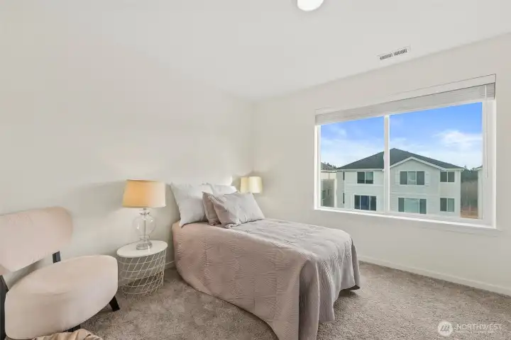 Light-filled bedroom with large window, soft neutral tones, and comfortable layout.