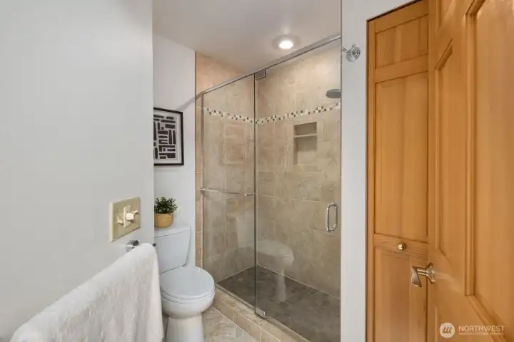 Tiled shower, toilet and linen closet for towels.