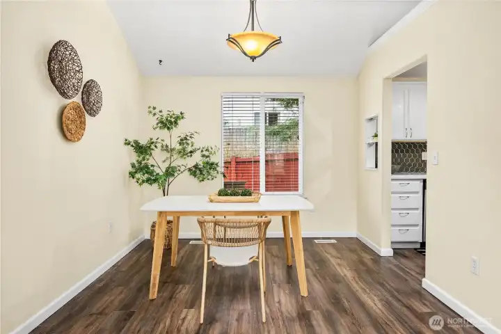 The dining room is filled with natural light from a large window overlooking the backyard and features durable wood-style flooring. An overhead fixture centers the space, while a decorative pass-through niche to the kitchen offers a perfect spot for displaying décor. The open doorway provides direct access to the updated kitchen, keeping this space functional and connected.