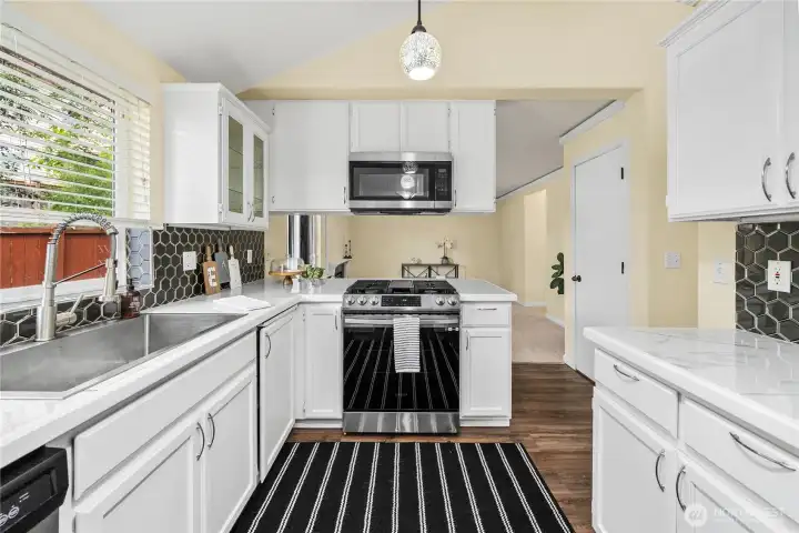Bright and functional, the kitchen features white cabinetry, updated countertops, and a modern tile backsplash. A large window above the sink provides natural light while overlooking the backyard.