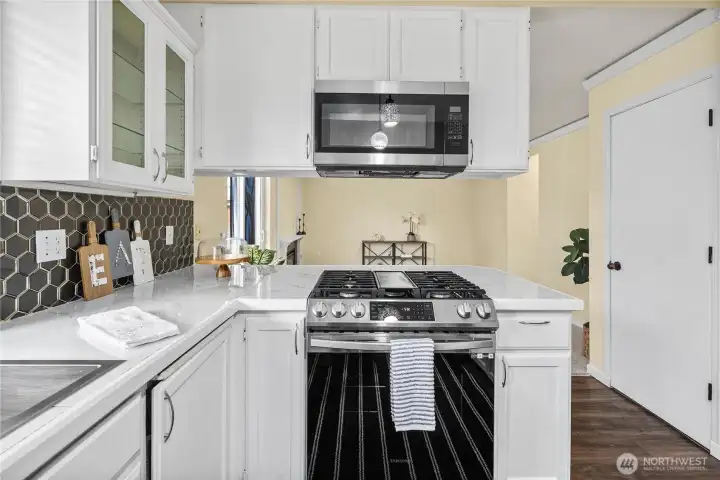 This angle highlights the gas range with overhead microwave and abundant counter space on either side. Crisp cabinetry and updated finishes create a clean, inviting cooking environment.