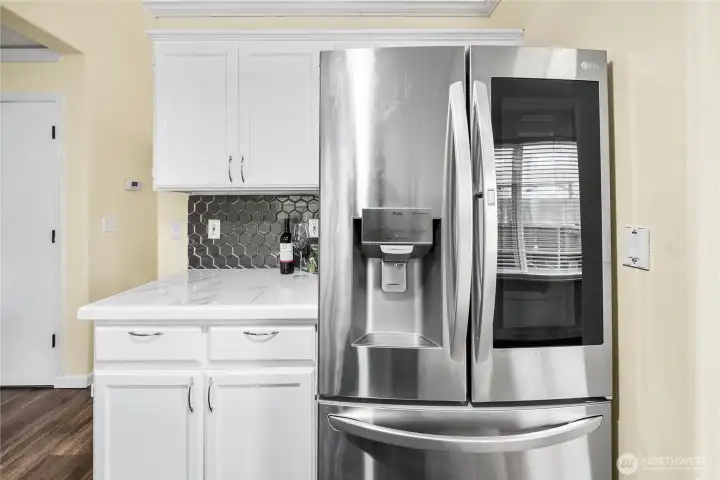 A stainless steel French-door refrigerator anchors this side of the kitchen, set against generous counter space and cabinet storage. The modern tile backsplash ties the design together.