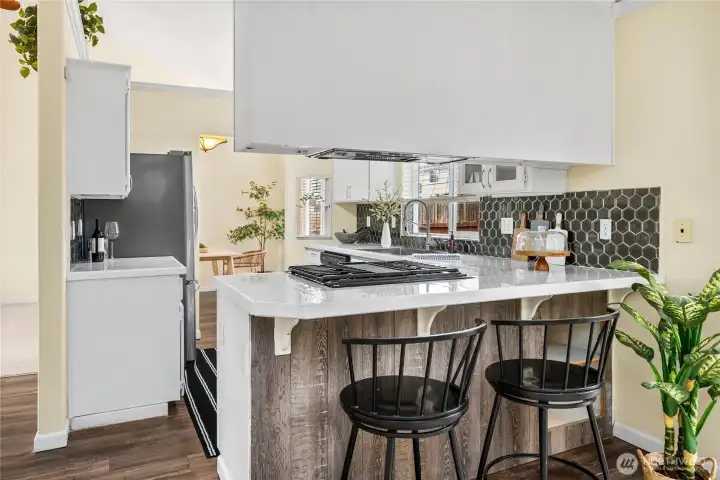 The kitchen opens with a peninsula breakfast bar, offering casual seating and additional prep space. A gas cooktop is built into the counter, complemented by a stylish tile backsplash and ample cabinetry.
