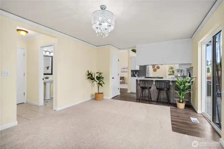 This perspective emphasizes the room’s versatility, with direct access to the half bath, kitchen, and outdoor area. Carpeted comfort and crown molding combine for a warm yet refined atmosphere.