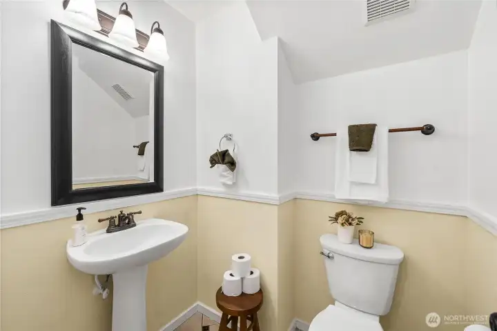 The convenient half bath on the main level features a pedestal sink, updated lighting, and a two-tone paint design with classic chair rail trim. Its central location makes it easily accessible for guests.