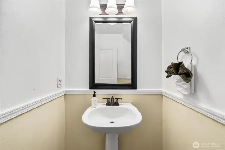 A closer look at the half bath highlights the pedestal sink and framed mirror under a stylish light fixture. Clean finishes and neutral tones create a fresh, functional space.