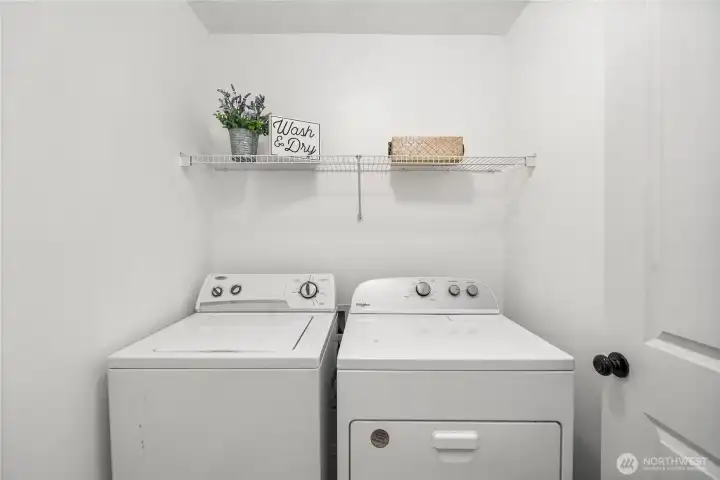 The dedicated laundry room offers convenience with washer and dryer included, plus a built-in wire shelf for storage and organization. Bright walls and a simple layout make this utility space efficient and functional.