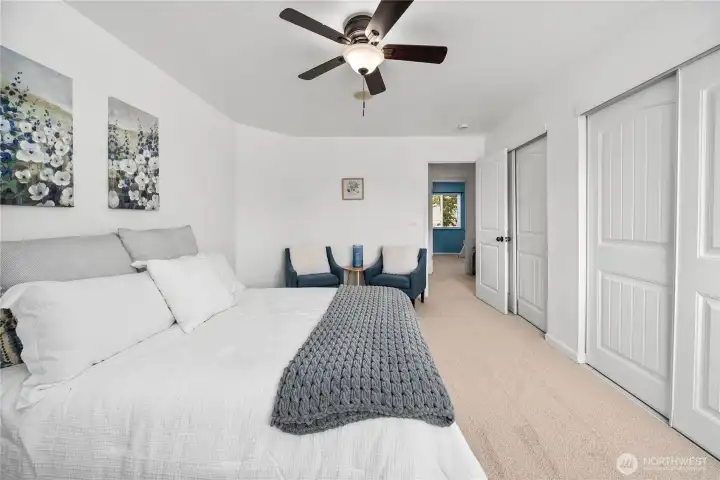 Another view of the primary suite highlights the expansive wall space and versatile layout, making it easy to accommodate a variety of furniture arrangements. Soft carpeting and a ceiling fan add comfort to this inviting space.