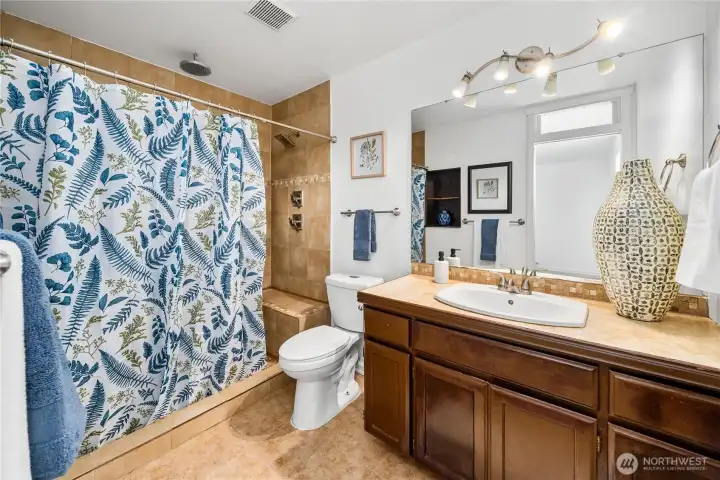 This full view of the primary bath highlights the combination of a large vanity, tiled shower, and practical layout. Warm finishes make it a comfortable and functional retreat.