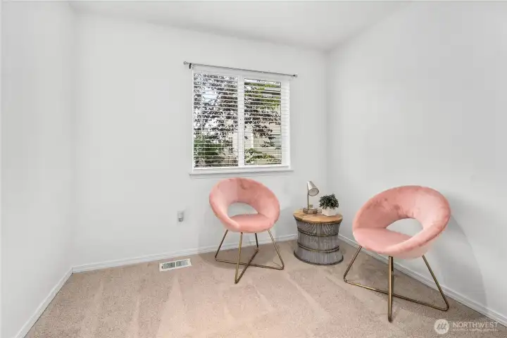 This bright bedroom features neutral walls and plush carpeting, creating a versatile space ready to serve as a guest room, office, or personal retreat. A large window brings in plenty of natural light while overlooking the backyard.