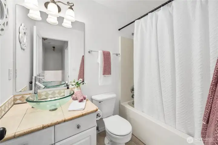 The full bathroom includes a tiled vanity with vessel sink, framed mirror, and updated lighting. A combination shower/tub with neutral finishes makes this space both stylish and functional for everyday use.