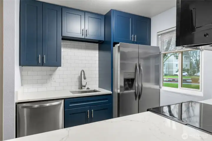 Fully renovated kitchen featuring quartz countertops, custom cabinets, stainless steel appliances, and tiled backsplash.