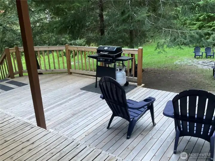 A generous, freshly finished deck extends the living space outdoors, complete with seating and grilling area, all set against a tranquil backdrop of greenery and towering evergreens for ultimate privacy. A generous, freshly finished deck extends the living space outdoors, complete with seating and grilling area, all set against a tranquil backdrop of greenery and towering evergreens for ultimate privacy.