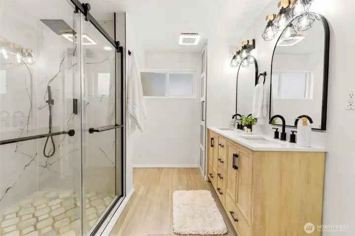 A beautifully remodeled spa inspired bathroom showcases a dual sink vanity, designer lighting, and contemporary finishes.