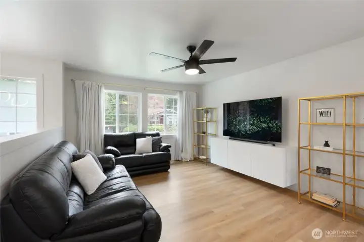 Bright living room featuring durable flooring, large windows for natural light, and a modern ceiling fan. Open, inviting space ideal for relaxing or entertaining.