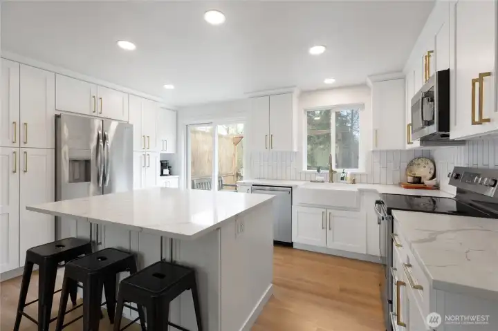 Fully remodeled kitchen featuring quartz countertops, custom cabinetry, and a spacious island with seating. Bright, modern finishes and updated appliances create a stylish and highly functional space.