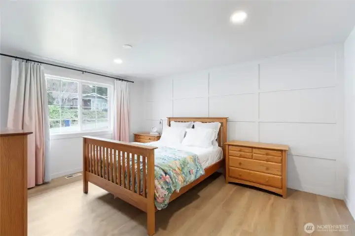 Private downstairs primary bedroom featuring updated flooring, recessed lighting, and a stylish paneled accent wall. Generous layout.