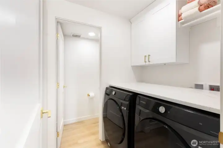 Laundry room conveniently located off the primary suite, offering abundant shelving, built-in storage, and quartz folding counter. Updated oversized Smart washer and dryer are included in the sale of this home.