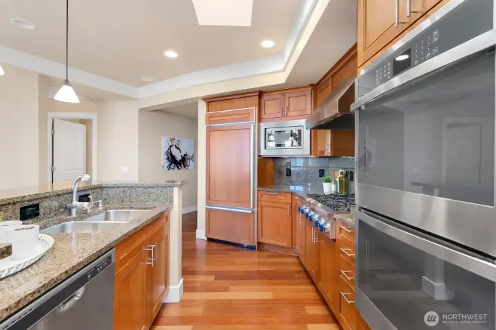 Well-appointed kitchen with stainless appliances, double oven, gas cooktop, warm wood cabinetry, and granite surfaces.
