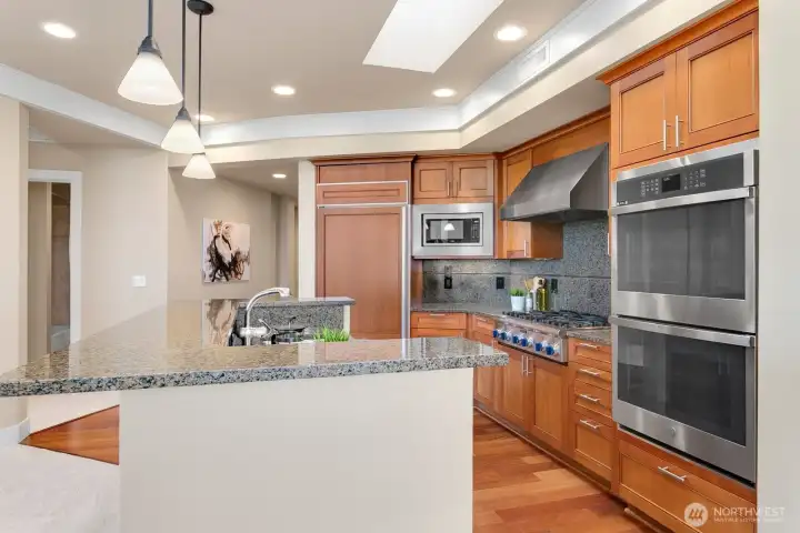 Kitchen detail featuring stainless appliances, gas cooking, double oven, warm wood cabinetry, and granite surfaces.