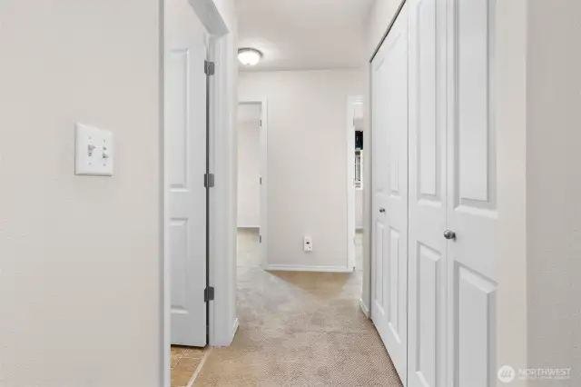 Standing at the top of the stairs, looking down the hallway with guest bathroom on left and laundry closet on right.