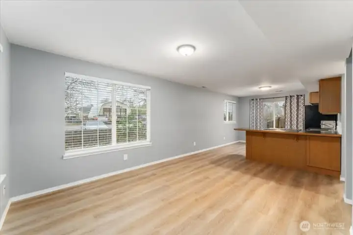 Living room and kitchen with LVP flooring and large windows overlooking the landscaped yard.