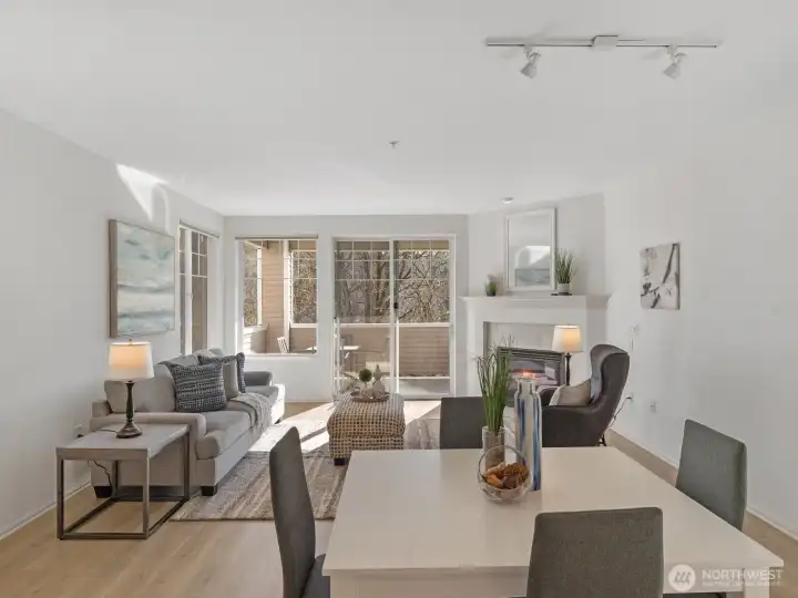 Open living and dining area with gas fireplace and large windows, connecting to covered deck and providing natural light and greenbelt views.
