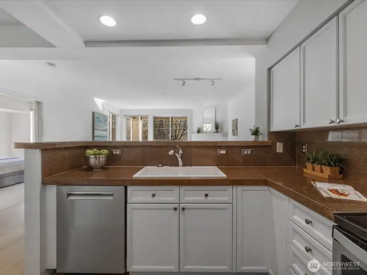 Kitchen with new sink, dishwasher, and pass-through opening to dining and living areas, supporting open-concept layout.