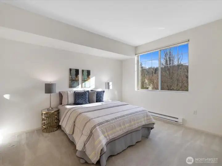 Bedroom with privacy, and large window providing natural light and views of surrounding greenery.