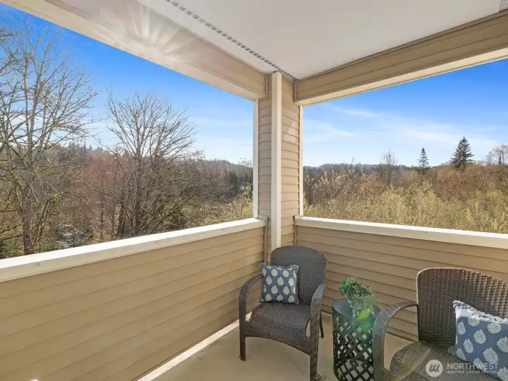 Covered corner deck overlooking wooded greenbelt with territorial views, providing outdoor space with year-round usability.