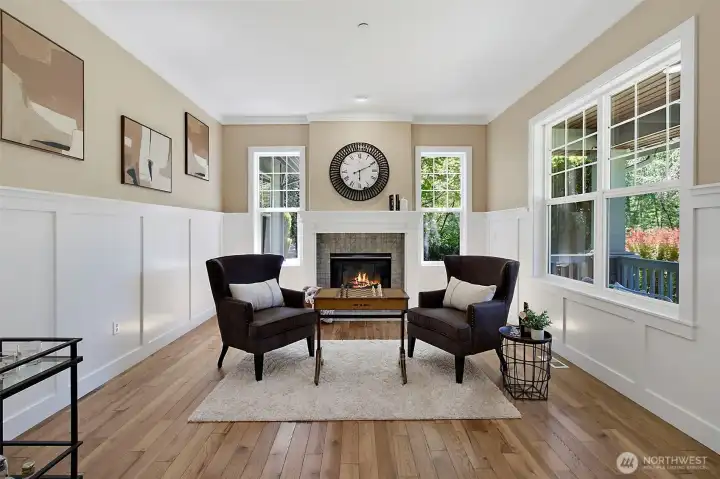 Formal sitting room with warm wood flooring, detailed trim work, large windows, and a cozy gas fireplace. Formal sitting room with warm wood flooring, detailed trim work, large windows, and a cozy gas fireplace.
