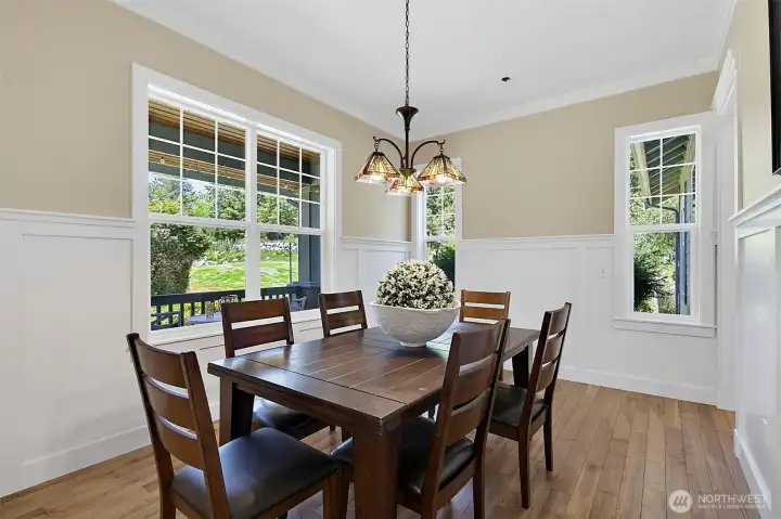 Formal dining room with warm wood flooring, detailed trim, upgraded lighting, and large windows overlooking the covered porch and greenery. Formal dining room with warm wood flooring, detailed trim, upgraded lighting, and large windows overlooking the covered porch and greenery.