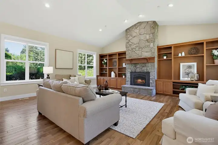 Family room with vaulted ceilings, warm wood flooring, built-in cabinetry, large windows, and a striking stone gas fireplace. Family room with vaulted ceilings, warm wood flooring, built-in cabinetry, large windows, and a striking stone gas fireplace.