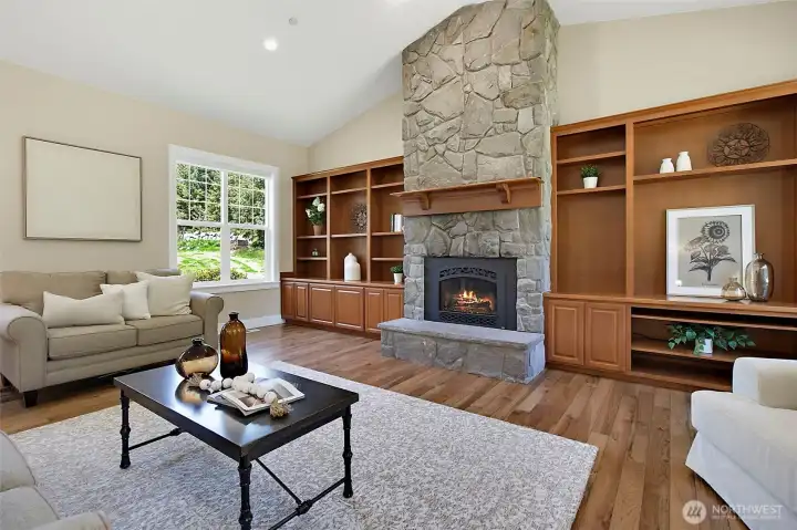 Family room with vaulted ceilings, warm wood flooring, built-in cabinetry, large windows, and a striking stone gas fireplace. Family room with vaulted ceilings, warm wood flooring, built-in cabinetry, large windows, and a striking stone gas fireplace.