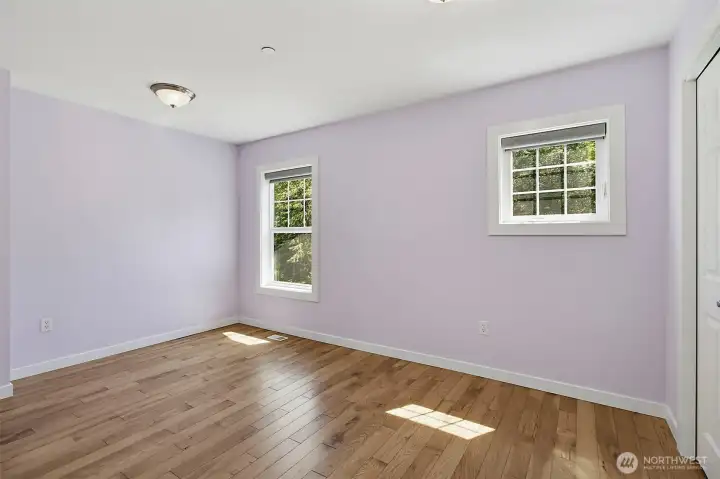 Bright bedroom with wood flooring, fresh paint, and peaceful views of the surrounding greenery. Bright bedroom with wood flooring, fresh paint, and peaceful views of the surrounding greenery.