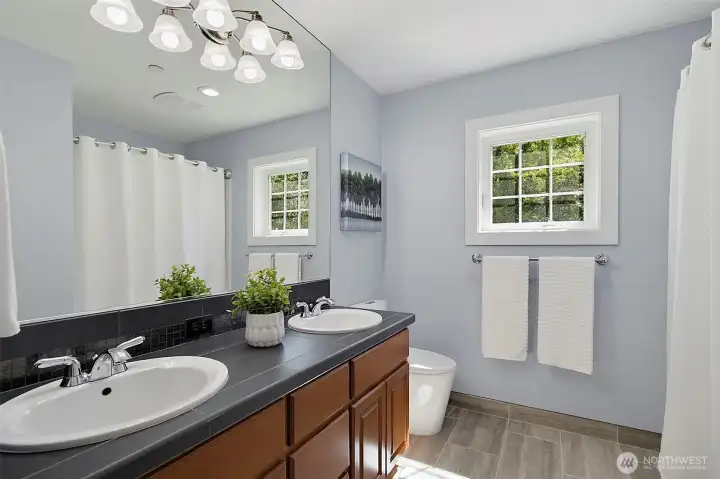 Full bathroom with dual sinks, tile flooring, and natural light from the window. Full bathroom with dual sinks, tile flooring, and natural light from the window.