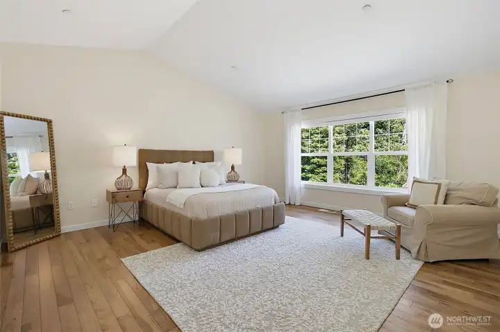 pacious primary bedroom with warm wood flooring, vaulted ceiling, and large window views of the private setting. pacious primary bedroom with warm wood flooring, vaulted ceiling, and large window views of the private setting.
