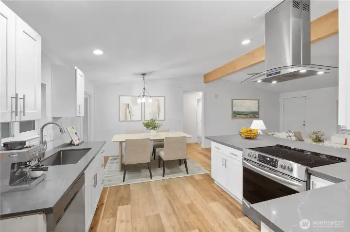 A bright, refreshed kitchen and dining area with white cabinetry, quartz-style counters, and warm wood flooring. The open layout flows easily into the dining space, which is styled to show how much room there is for everyday meals or entertaining. Clean lines, modern lighting, and natural light create a welcoming central hub of the home.